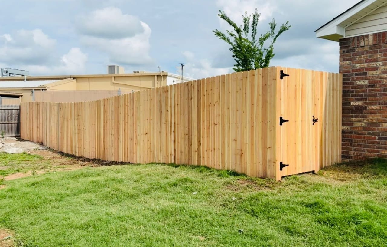 Freshly built cedar privacy fence with a matching swing gate and black hardware along the side of a brick home