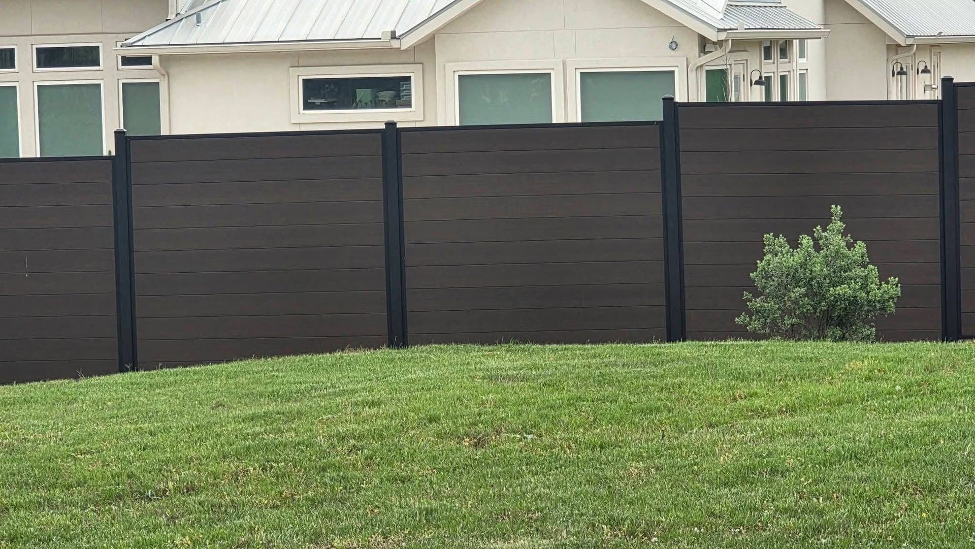 Tall dark composite privacy fence with black aluminum posts installed behind a modern white farmhouse in Northeast Oklahoma