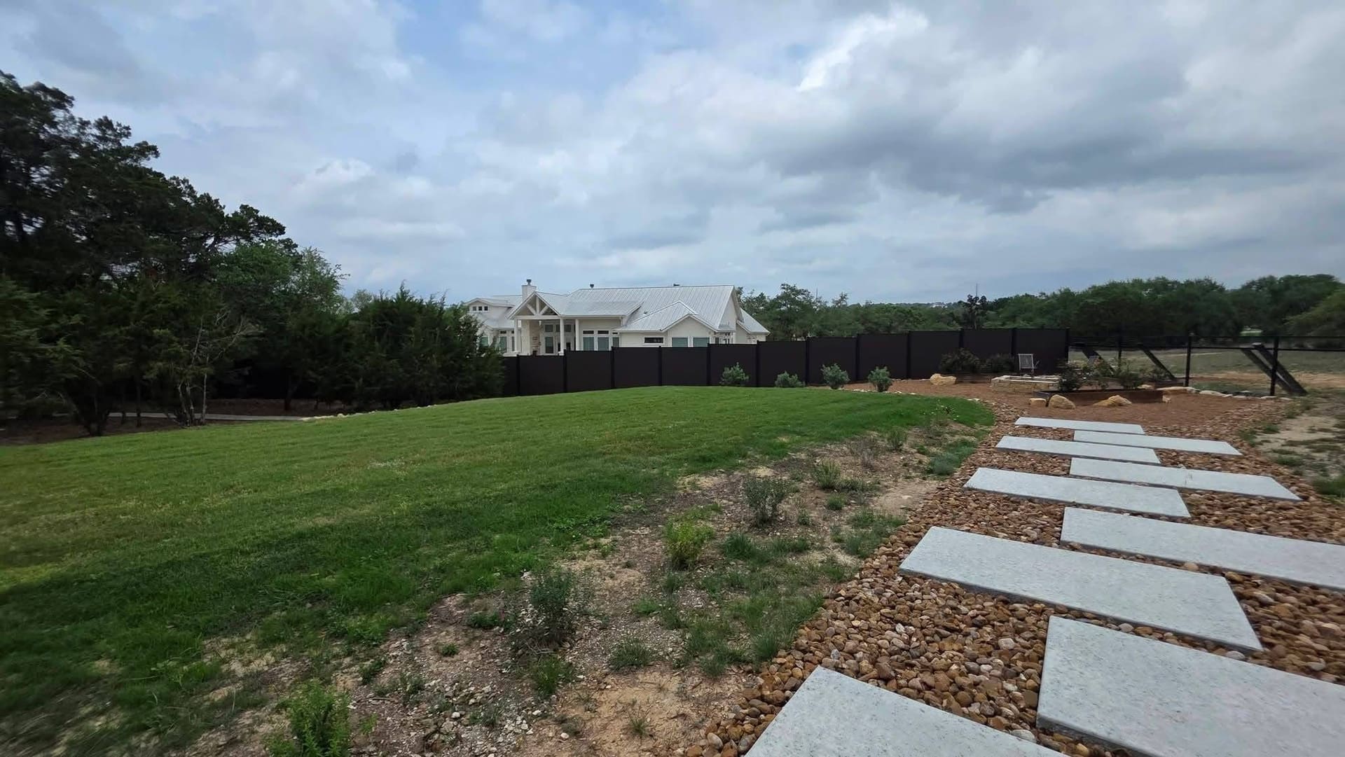 Long run of black composite privacy fencing enclosing a large rural property with a white ranch home in the distance