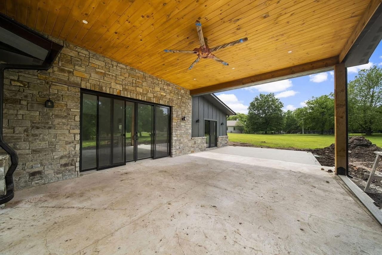 Covered outdoor living patio with stone columns, a stained tongue-and-groove wood ceiling and black sliding glass doors