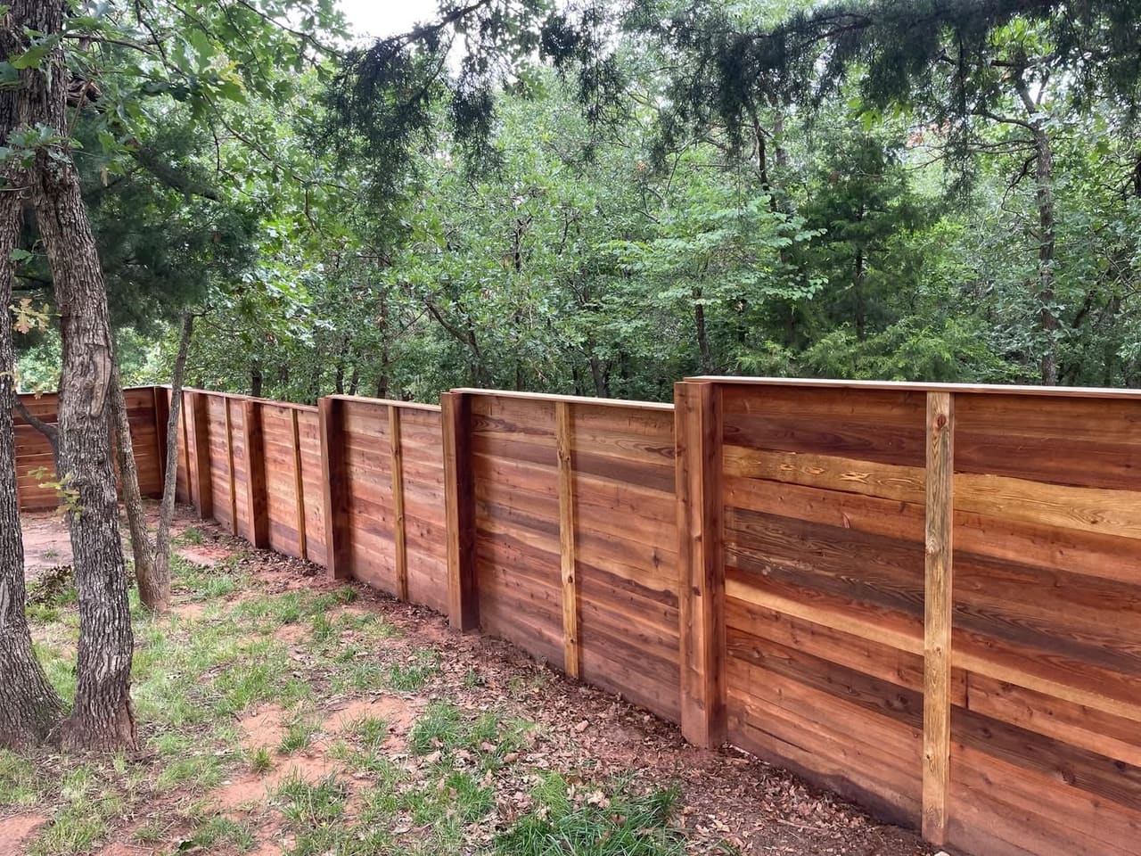 Long horizontal-board cedar privacy fence stepping down a wooded, tree-lined lot