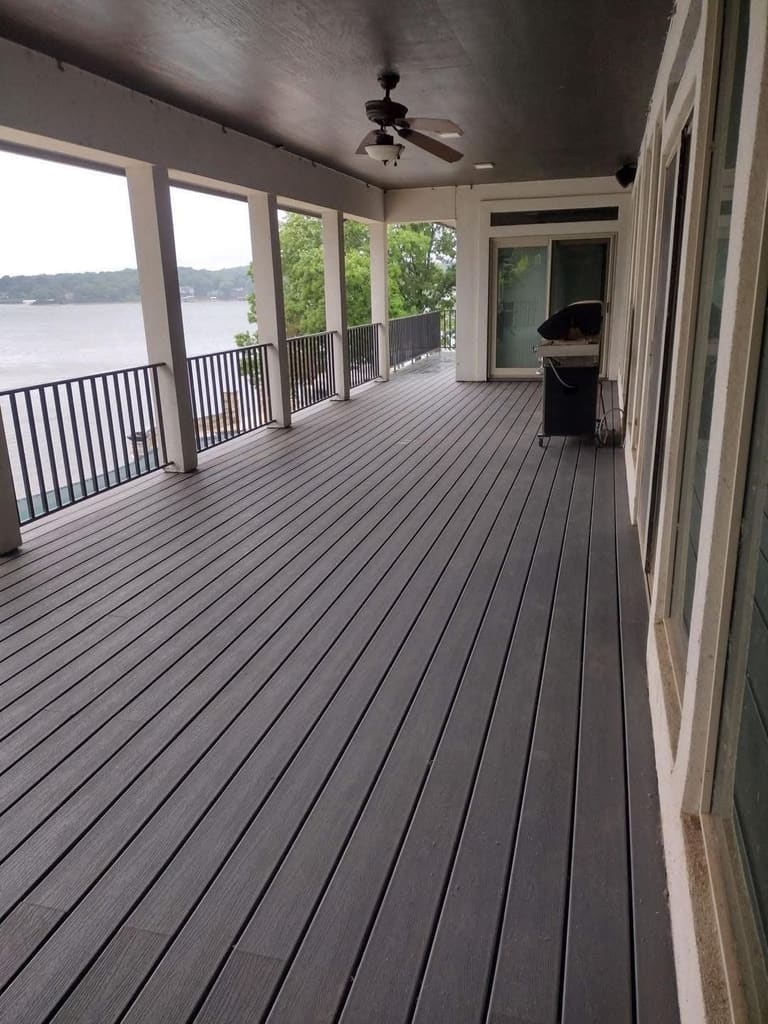Covered composite deck with a ceiling fan and black metal railing overlooking the lake